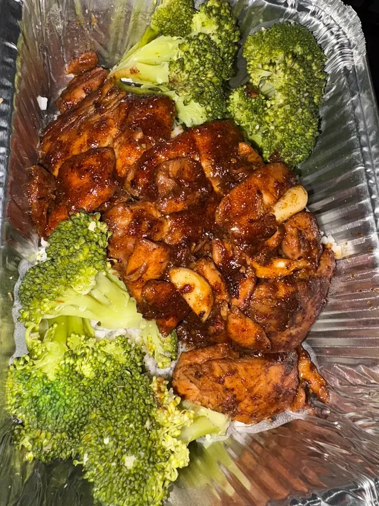Chicken and broccoli meal in a foil container. Brown chicken with sauce, green broccoli.