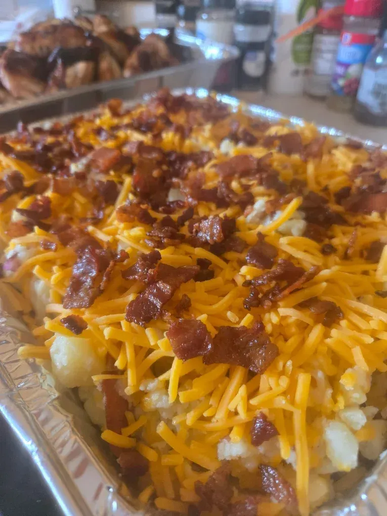 Loaded potato casserole in a foil pan, topped with shredded cheese and bacon.