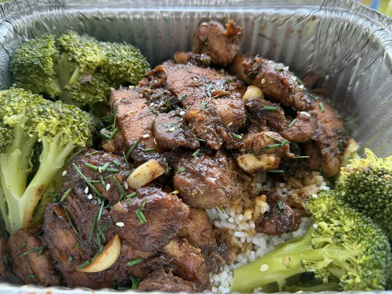 Meal with broccoli, meat, rice, and garlic in a foil container.