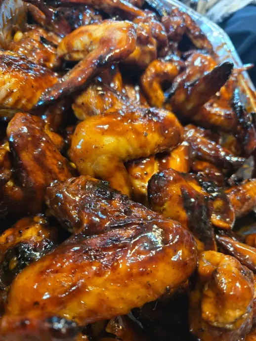 Close-up of a pile of glazed chicken wings, glistening with dark brown sauce.