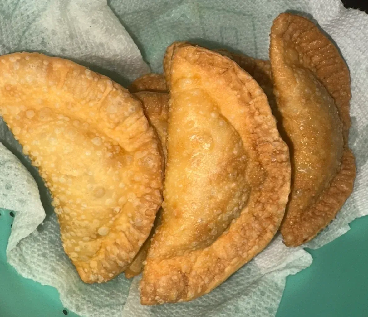 Golden-brown, fried pastries, likely empanadas, rest on a paper towel-lined plate.