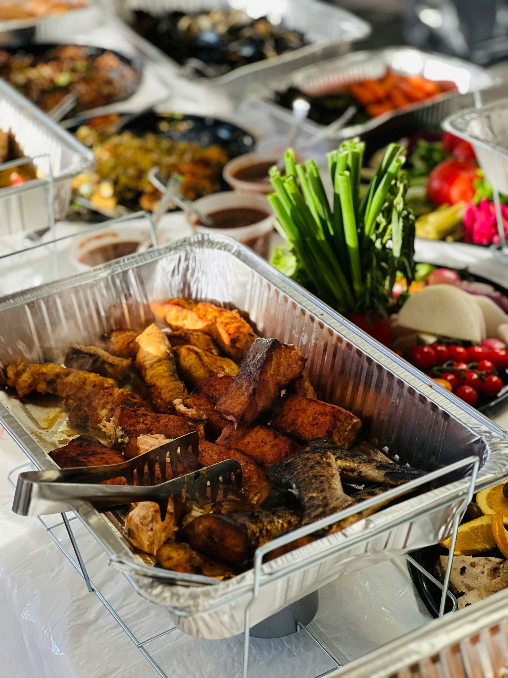 Buffet with various dishes: grilled salmon, vegetables, and other unidentified food.
