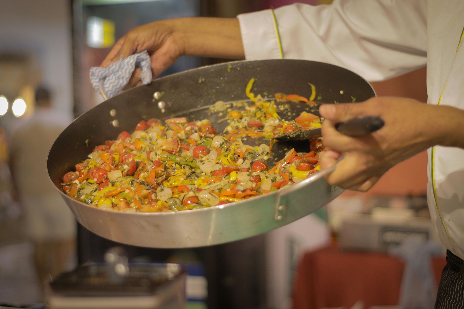 Chef holding a large pan with cooked vegetables, likely for a dish, in a restaurant setting.