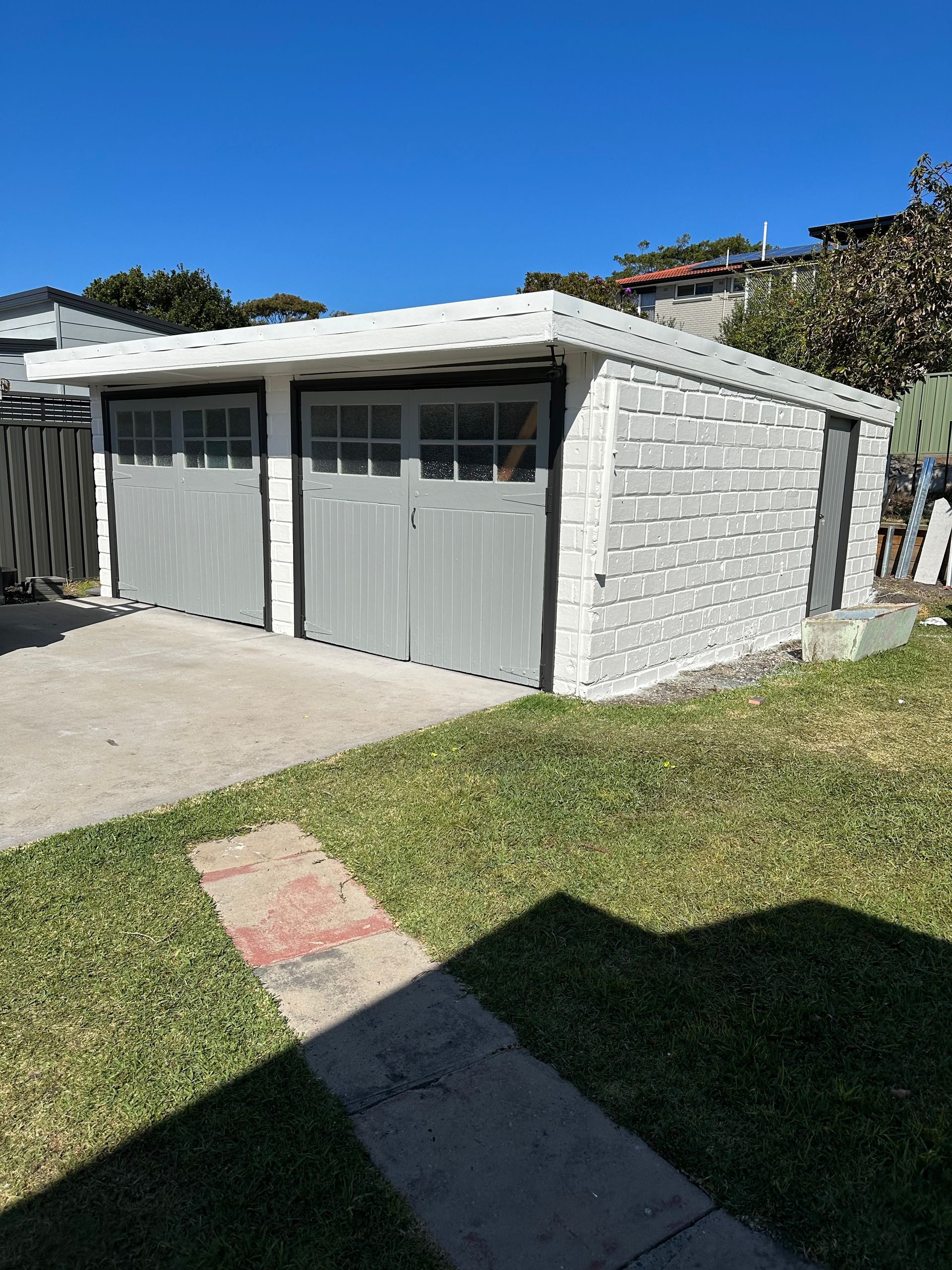 A white brick garage with gray garage doors in a backyard — Blake Saunders Painting In Edgeworth, NSW