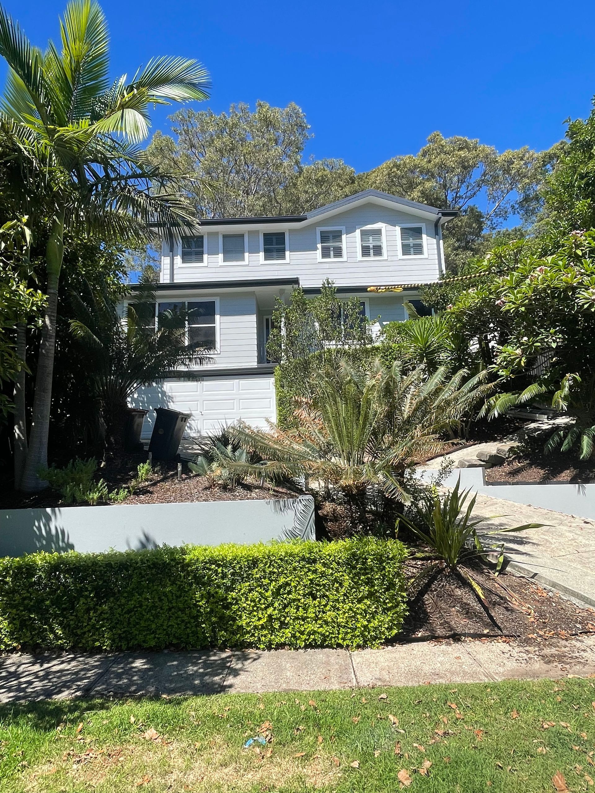 A large white house with a lot of windows is surrounded by trees and bushes — Blake Saunders Painting In Edgeworth, NSW