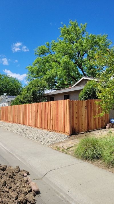 A wooden fence is sitting on the side of a road next to a house.