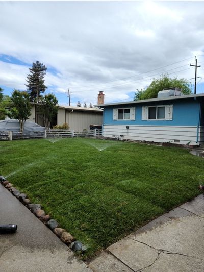 A house with a large lawn and a sprinkler in front of it.