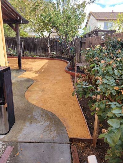 A backyard with a concrete walkway and a fence.