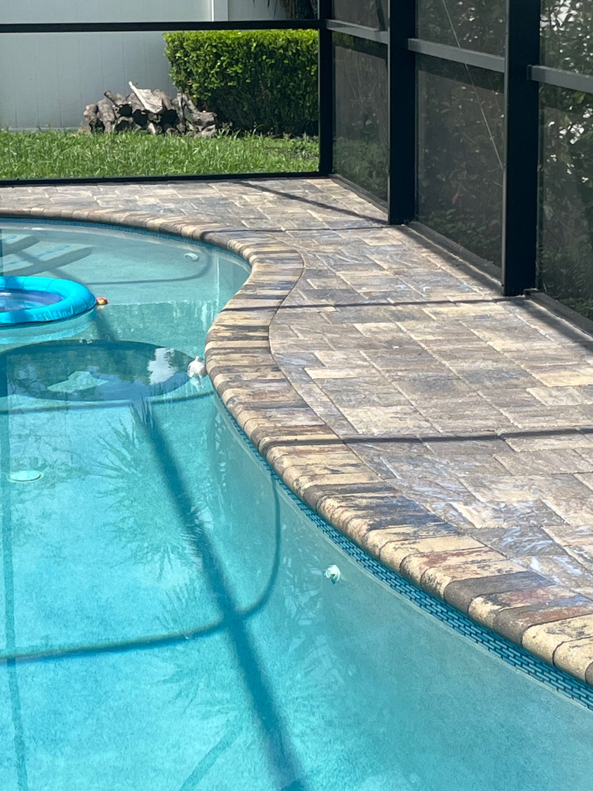 Poolside view with stone pavers, blue water, and a screen enclosure.