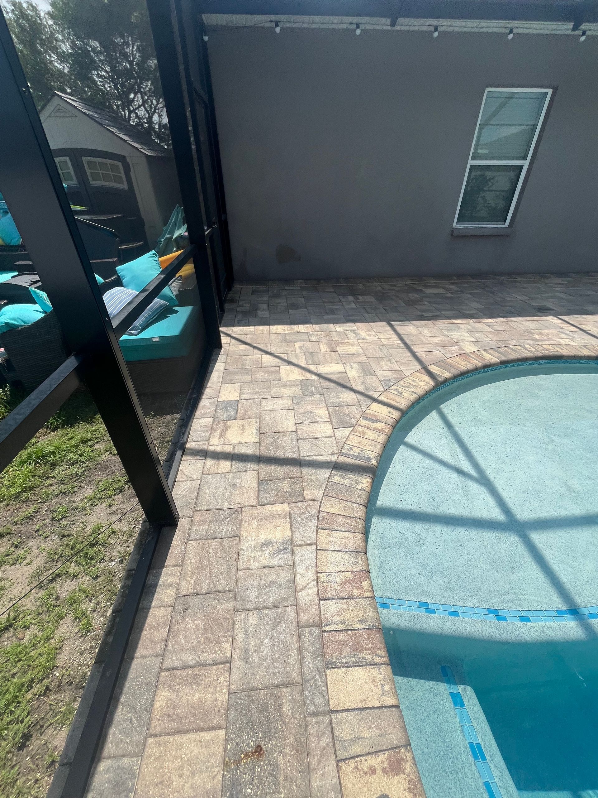 Poolside patio with patterned pavers, black screened enclosure, and turquoise pool water.