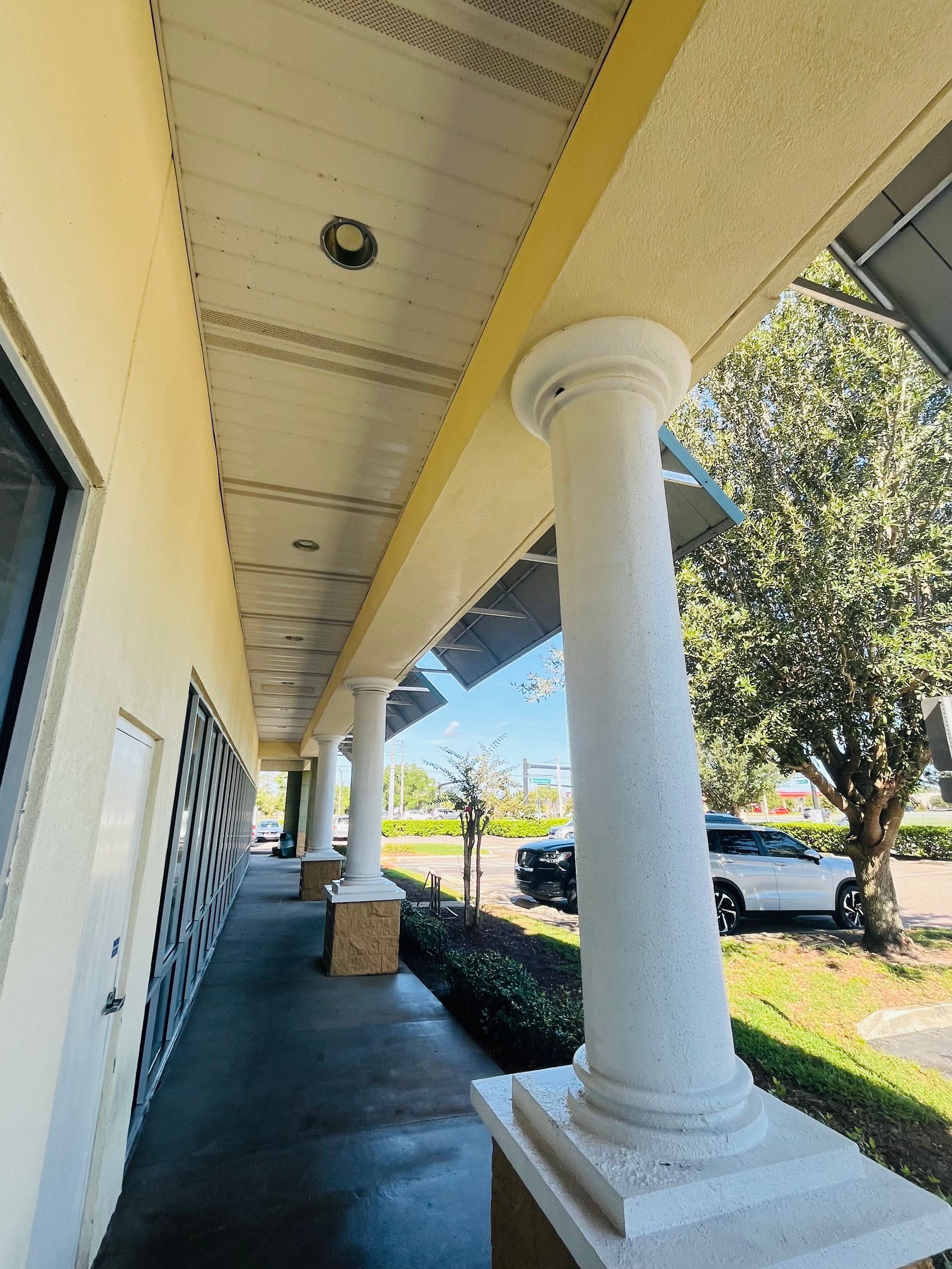 Exterior view of a building with white columns, a sidewalk, and a row of windows along the side.
