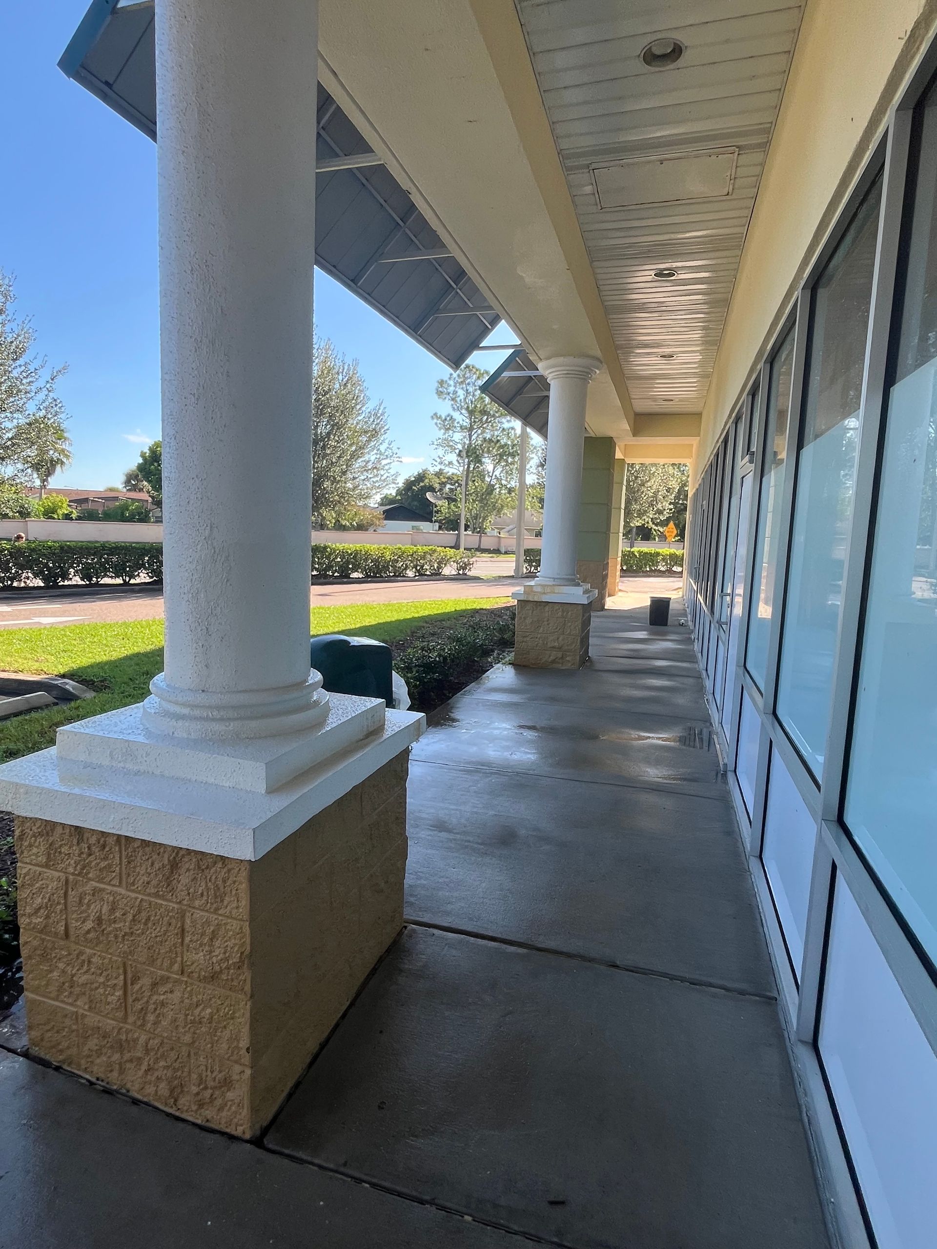Covered walkway with columns, windows, and landscaping; exterior of a building.