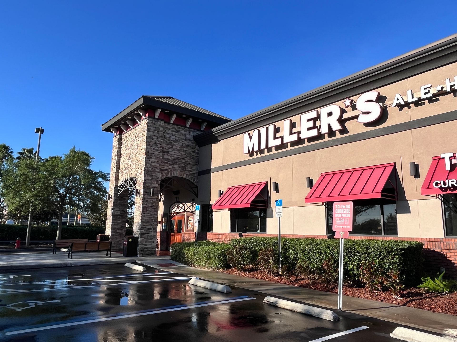 Miller's Ale House restaurant with stone facade and red awnings; wet parking lot on a sunny day.