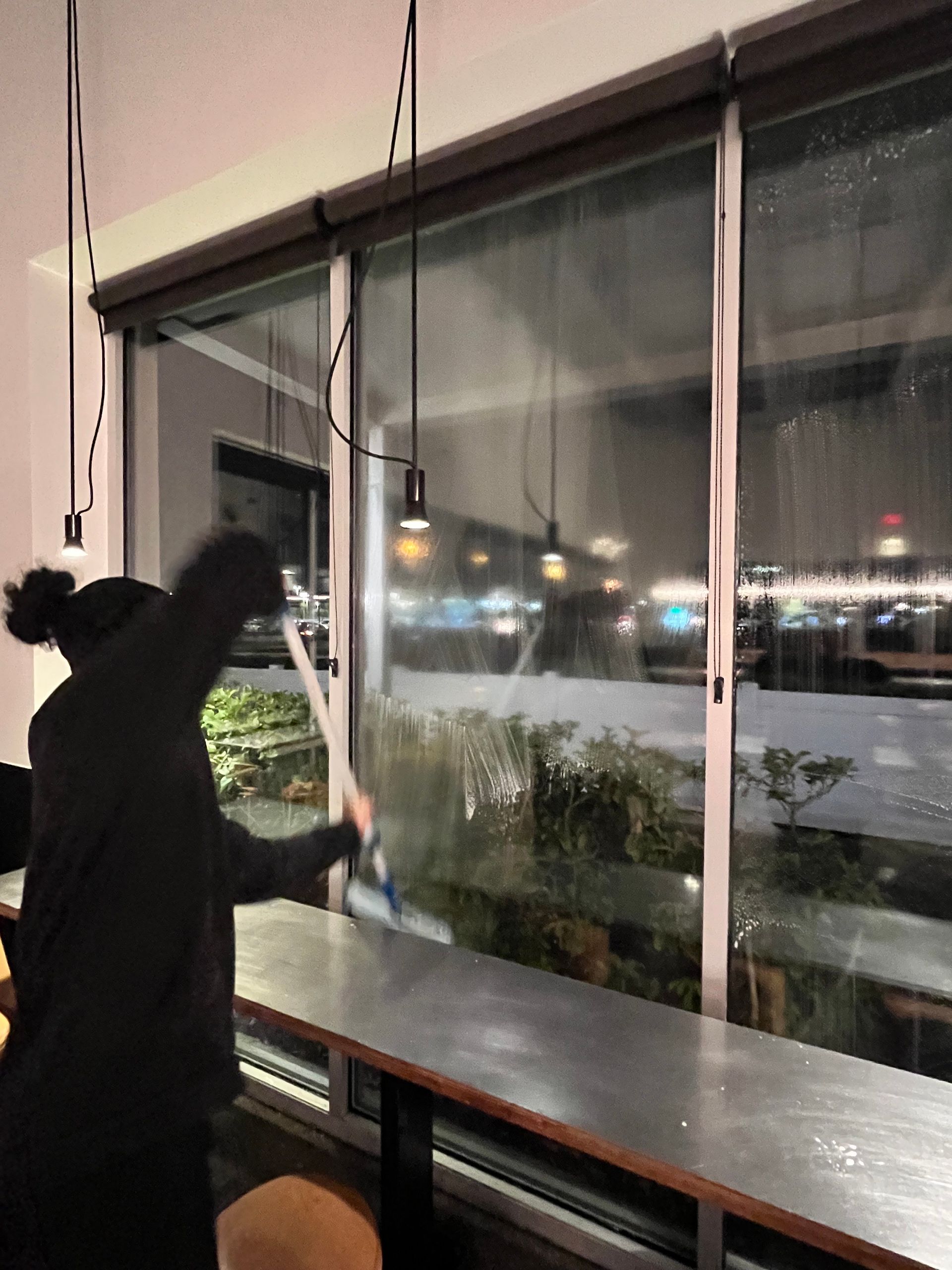 Person cleaning a window in a cafe, view of snowy outdoors, black pendant lights.