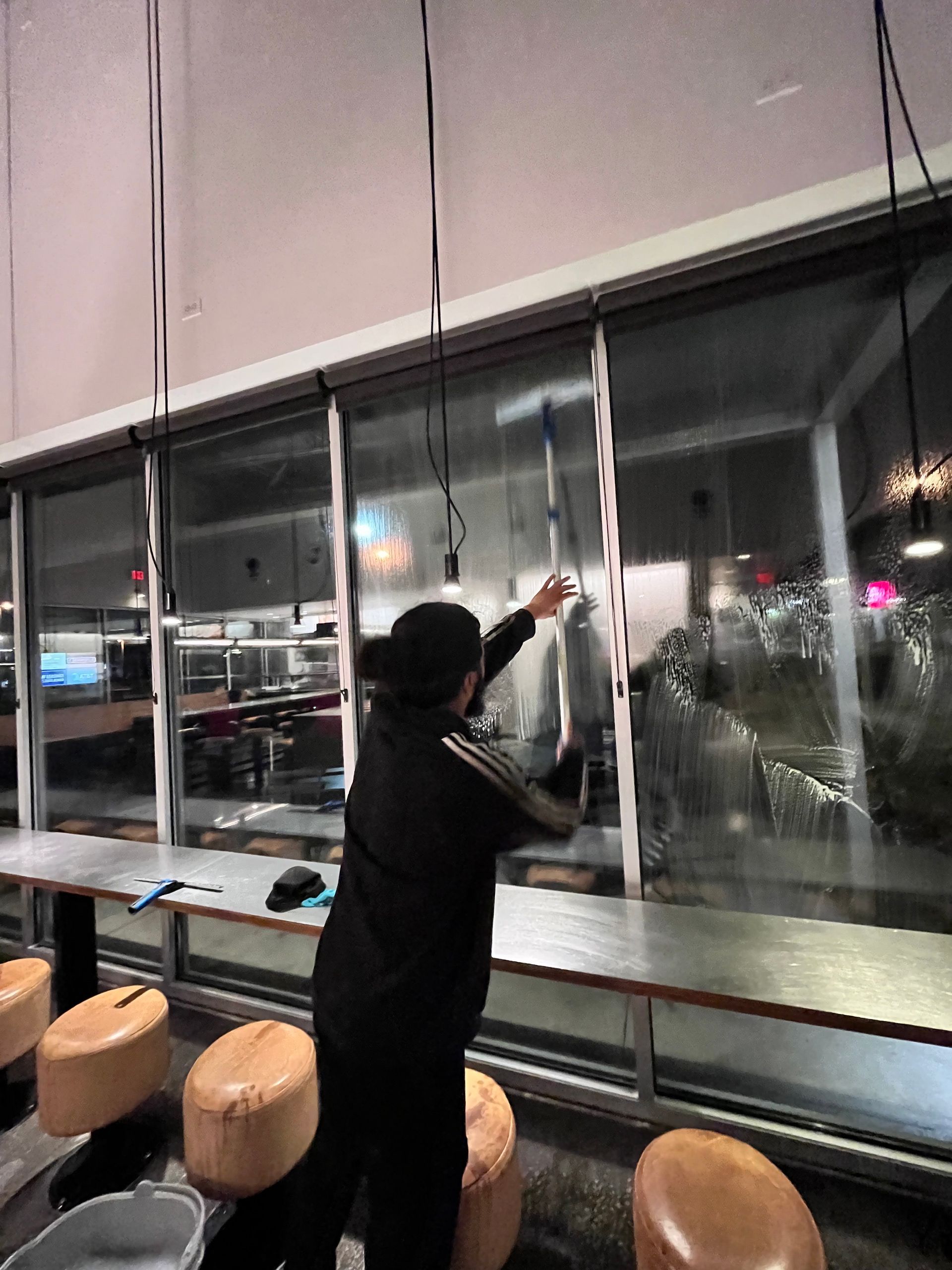 Person cleaning window in a commercial space; they are wearing black and using a squeegee.