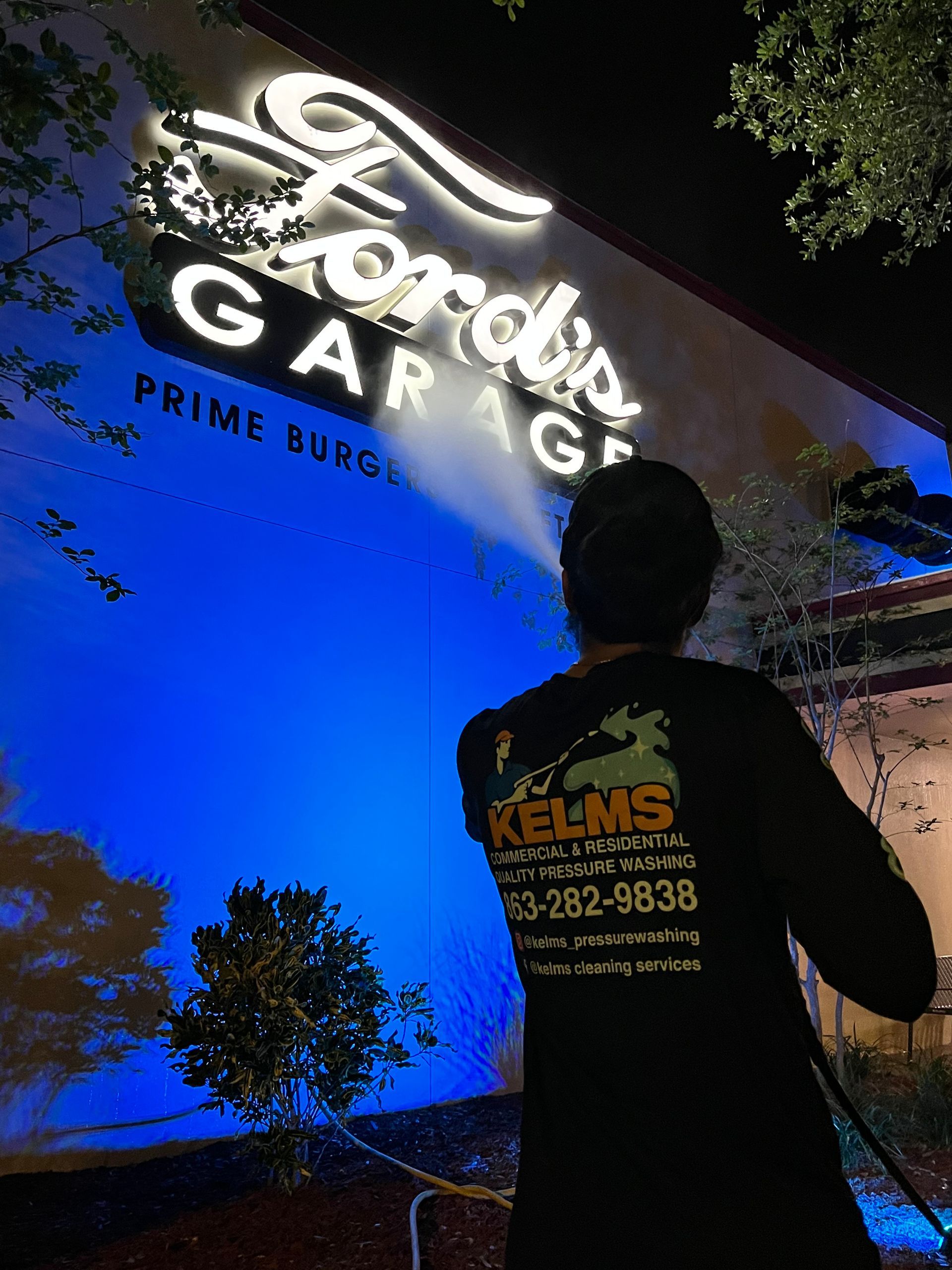 A person power washes the blue wall of Ford's Garage restaurant at night.