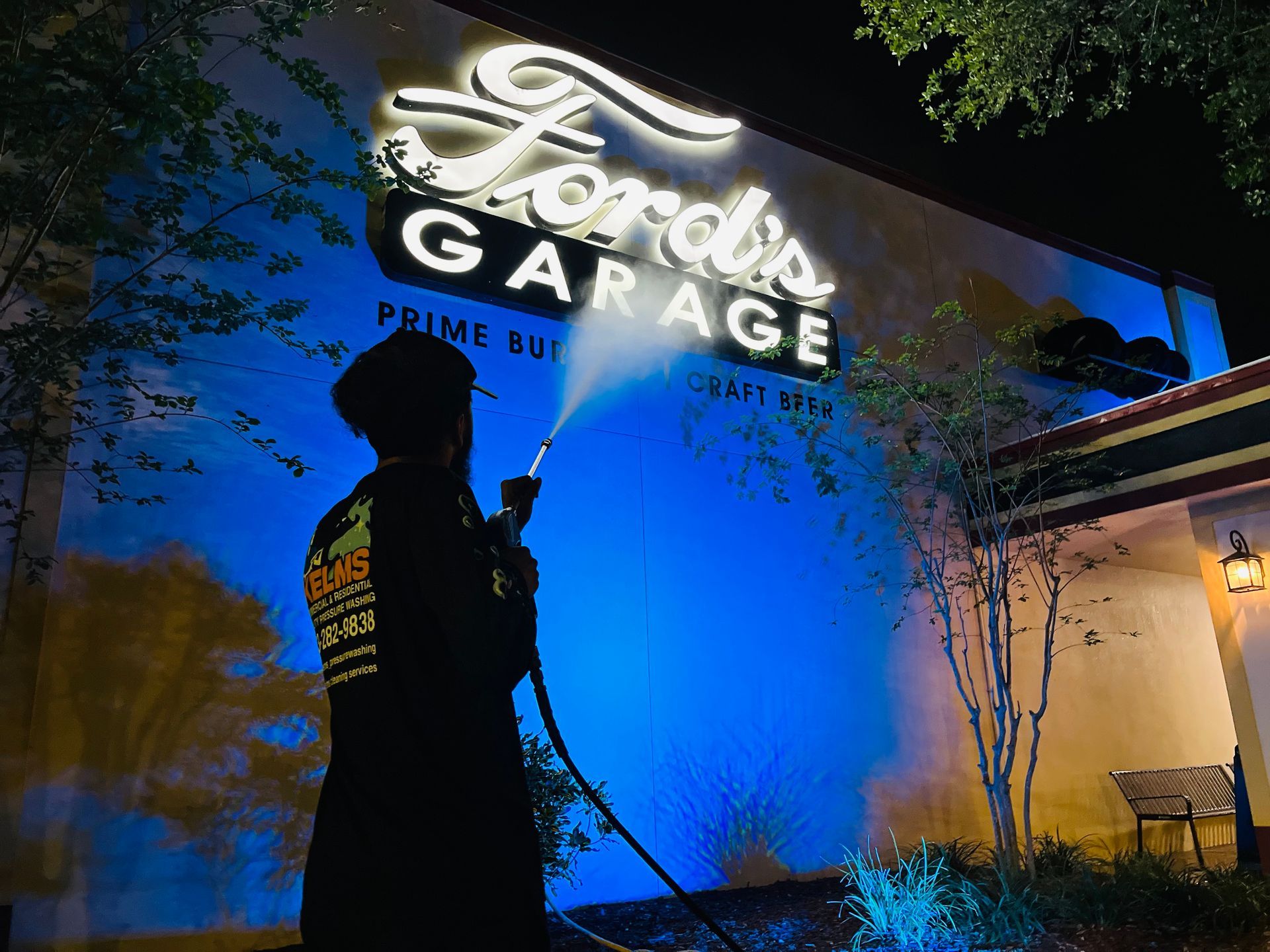 Person spraying water at the lit sign of Ford's Garage restaurant at night.