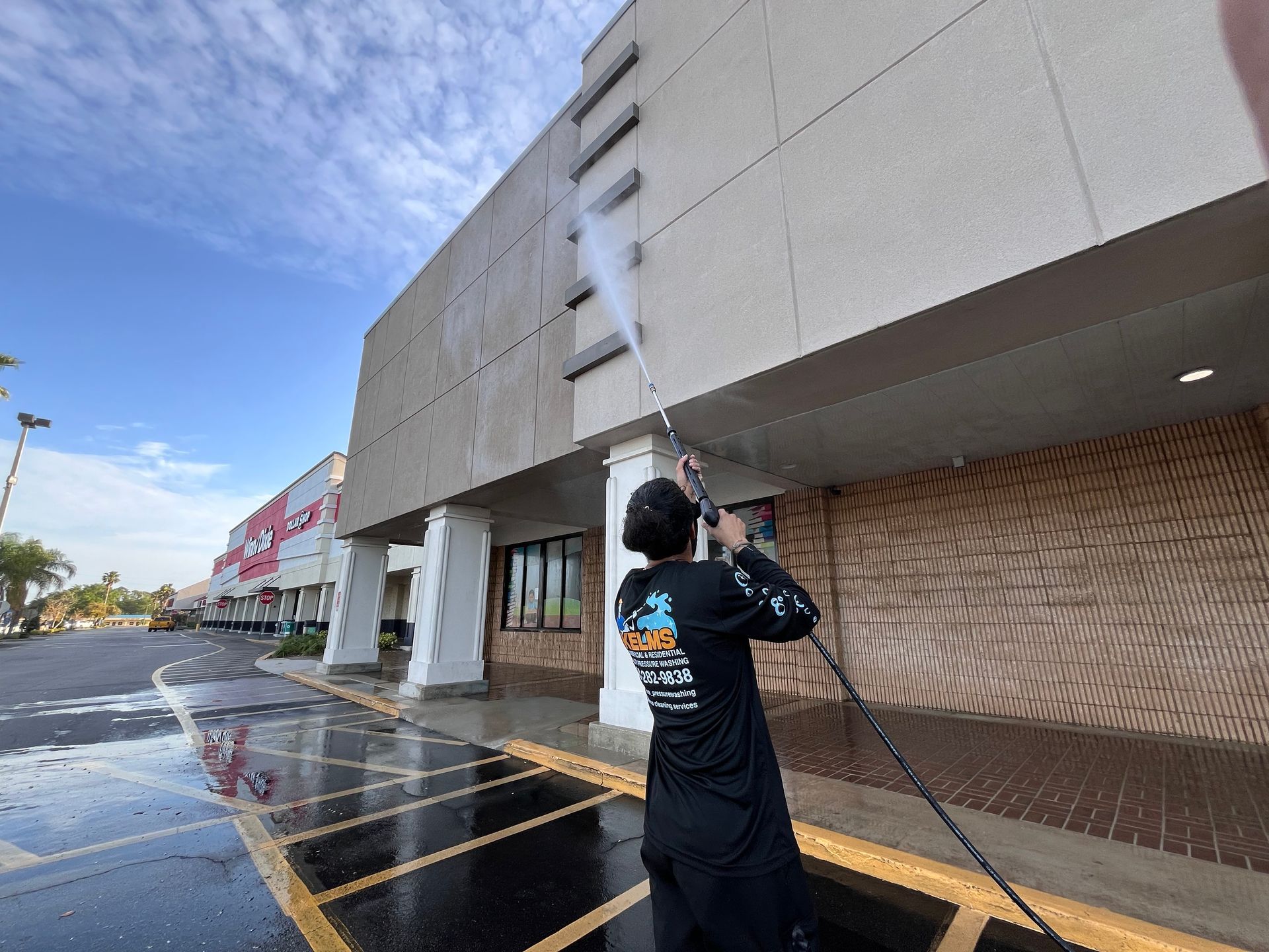 A person power washing the exterior of a commercial building on a sunny day.