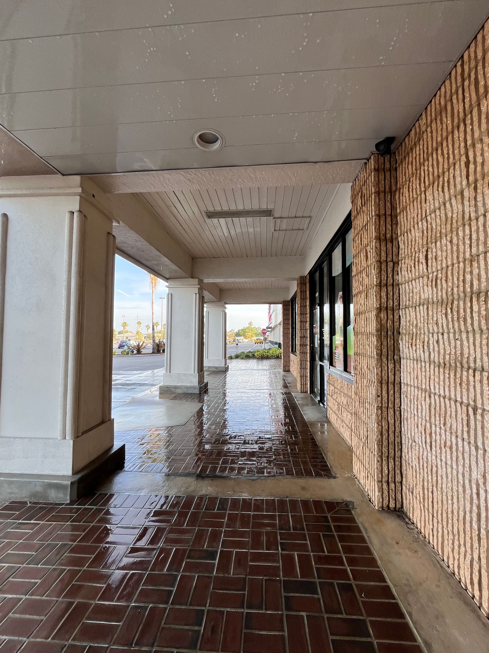 Covered walkway with columns and a textured brick wall, wet from recent rain.