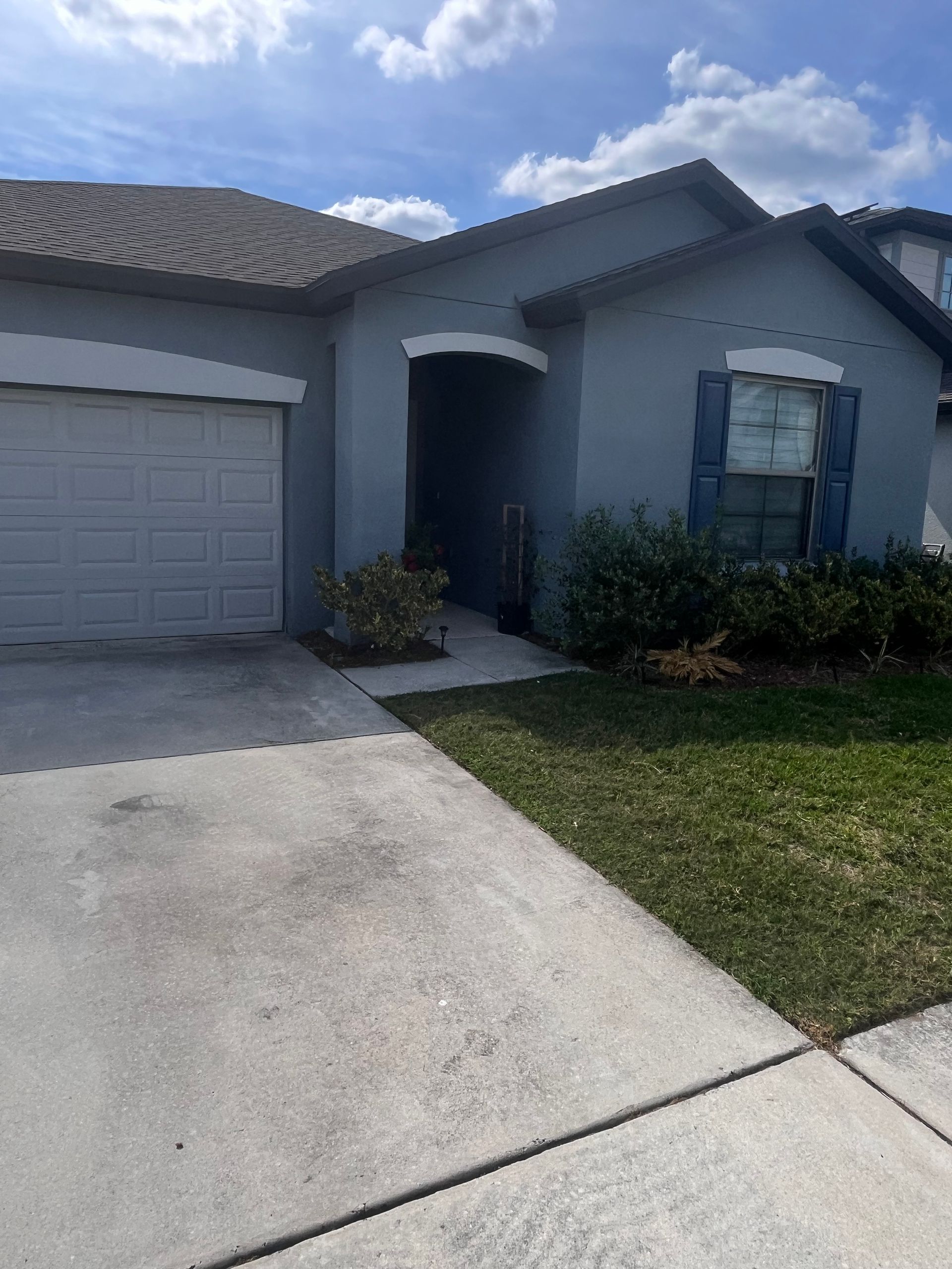 Blue house with a gray garage door and driveway on a sunny day.