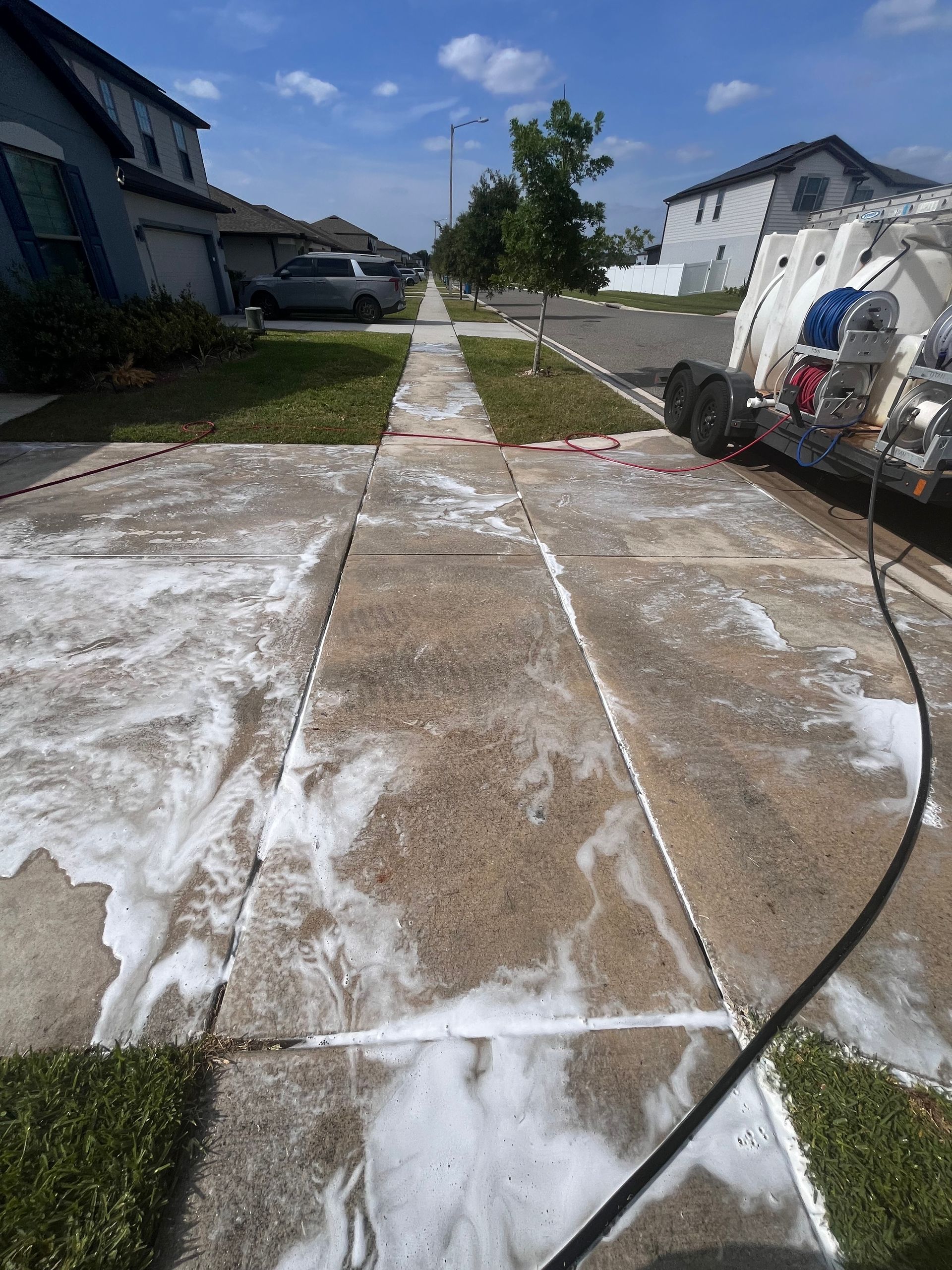 Sidewalk being pressure washed with soapy water. Exterior setting, sunny day.