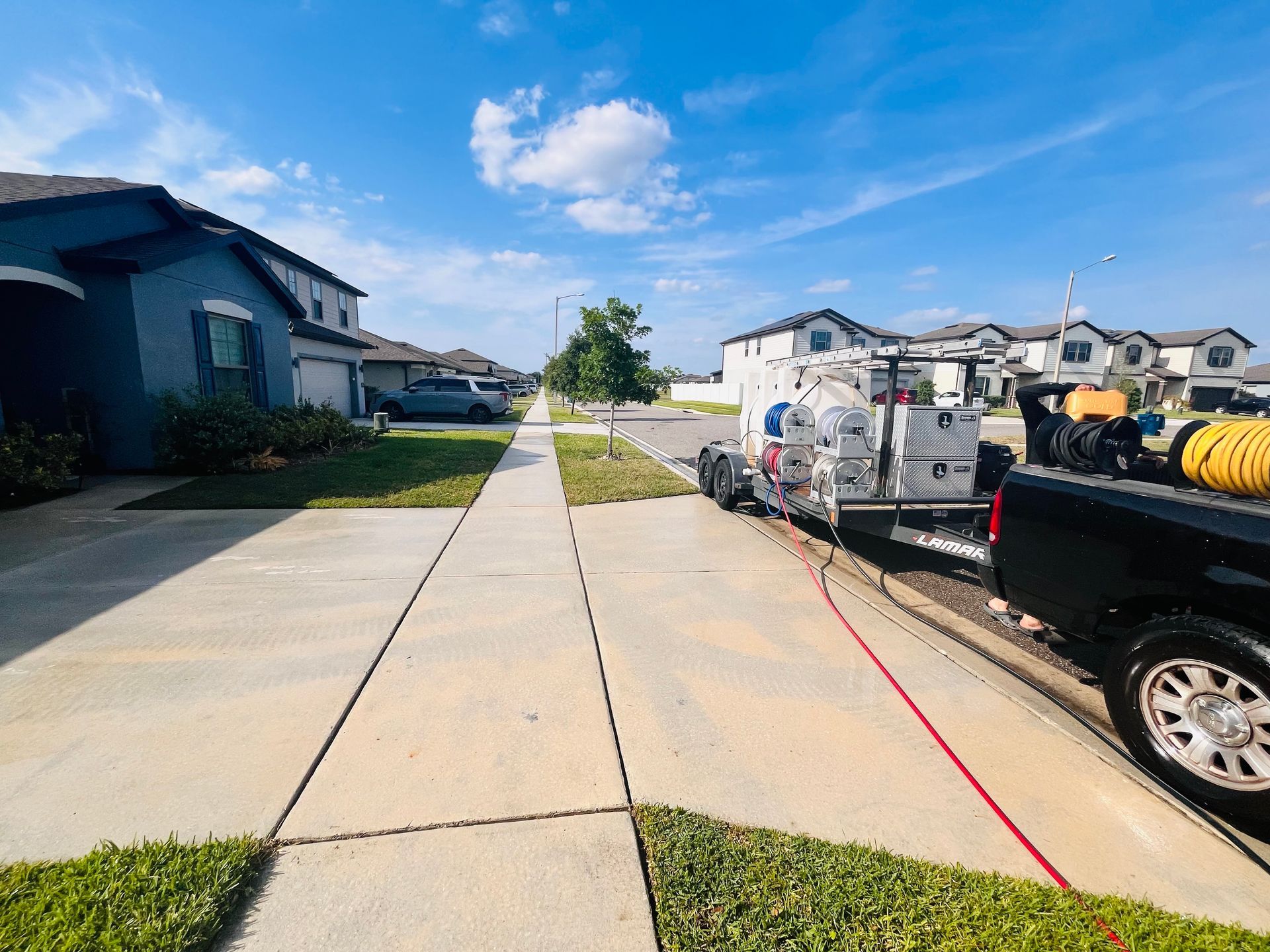 A truck with cleaning equipment parked on a sidewalk, in a suburban neighborhood on a sunny day.