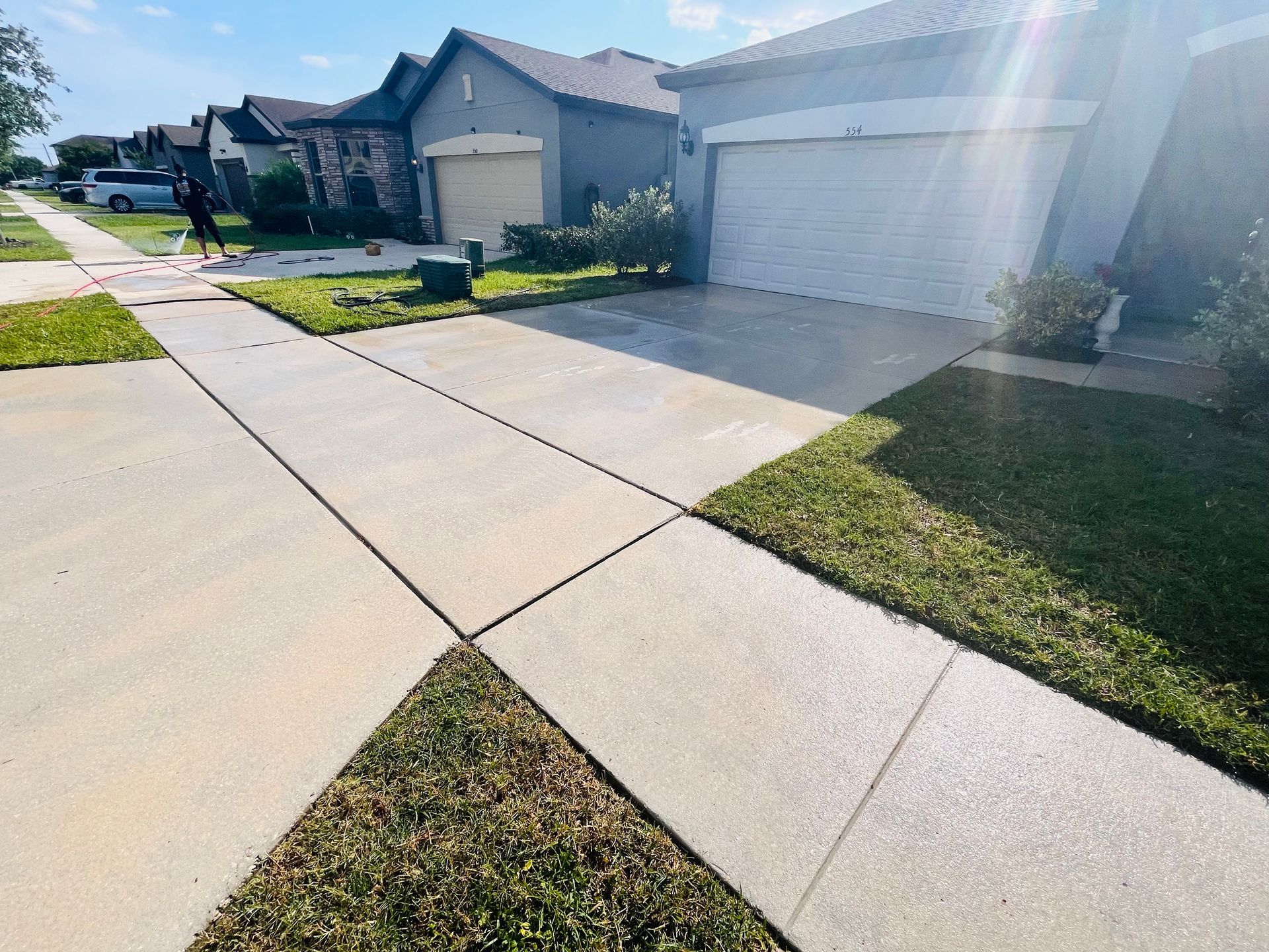 Sidewalk and driveways in a suburban neighborhood, with a person walking a dog in the background.