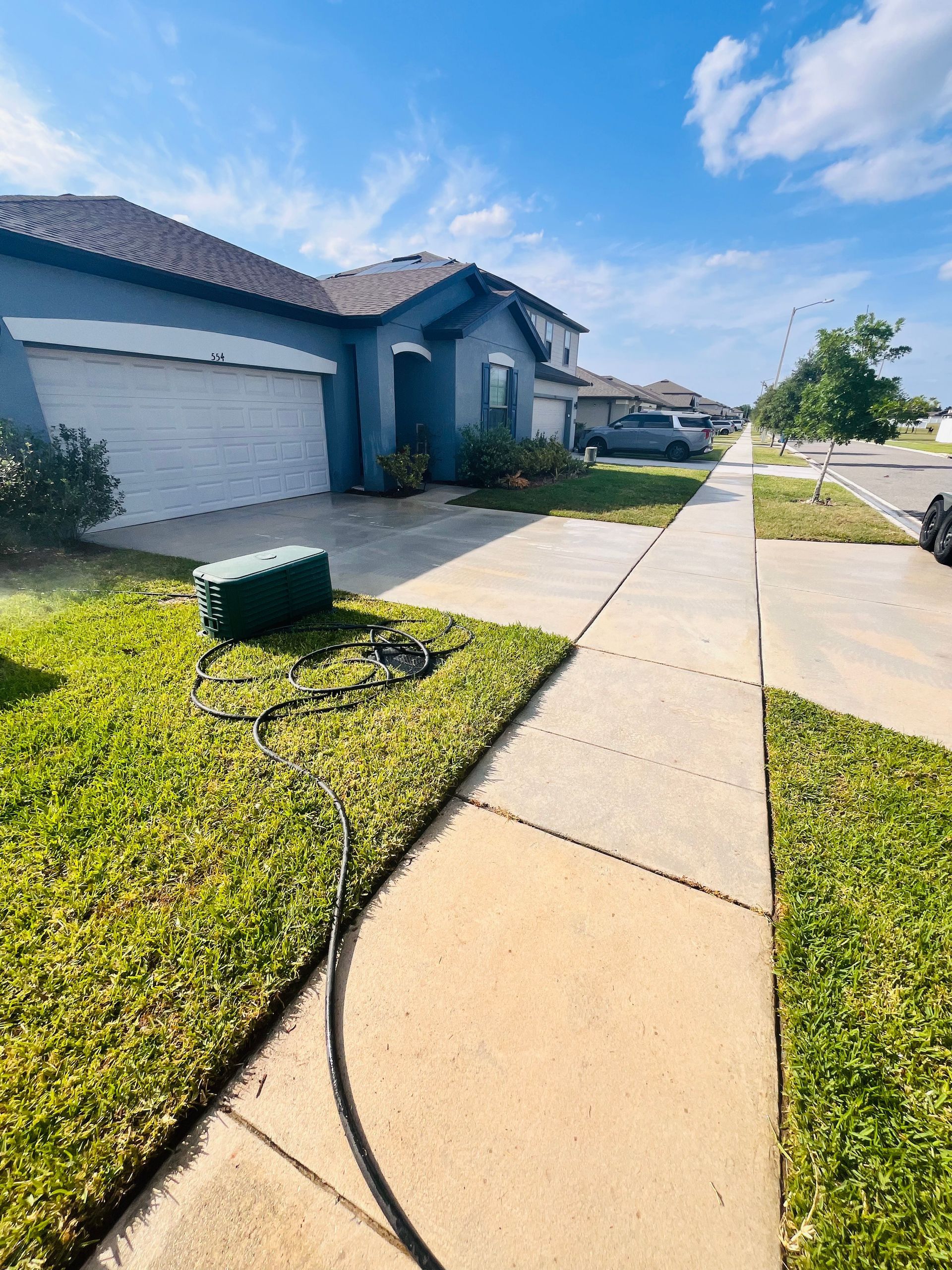 A person pressure washing a driveway in front of a blue house on a sunny day.