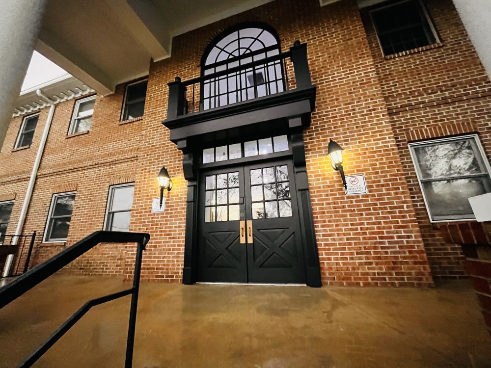 Brick building entrance with black double doors, balcony, and porch lights.  A black handrail leads up to the entrance.