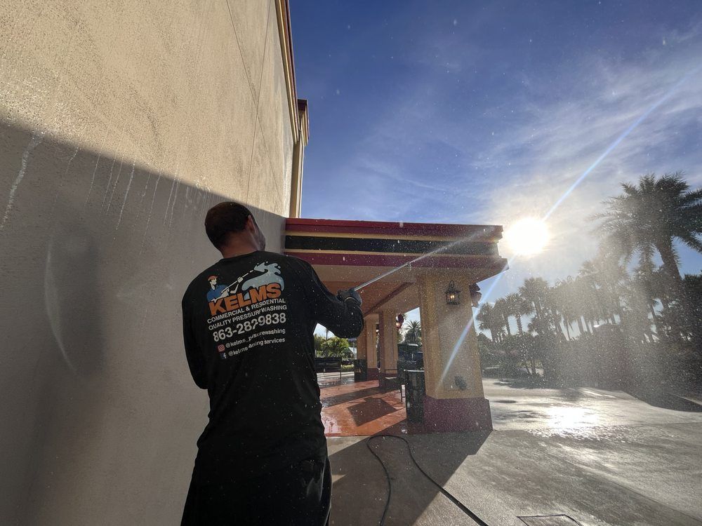 A man power washes the exterior of a building with sunlight shining in the background.