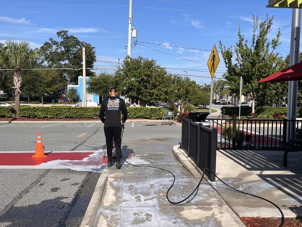 Person power washing a sidewalk near a McDonald's.  A red painted area and an orange traffic cone are nearby.