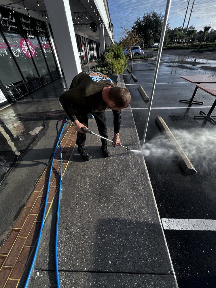 Person power washing a sidewalk in front of a building, creating a plume of mist.