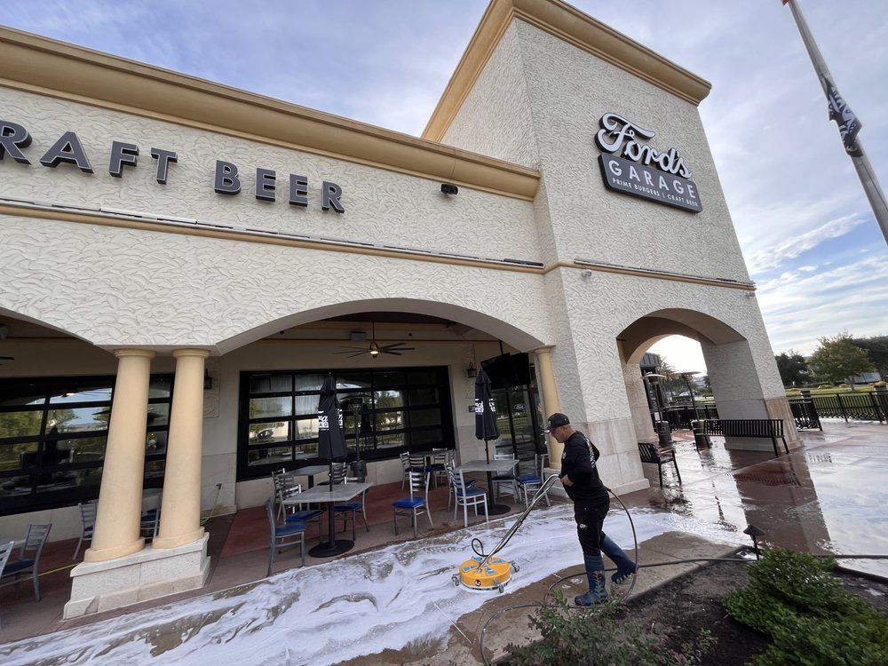 A person power washes the sidewalk in front of a restaurant with the sign 