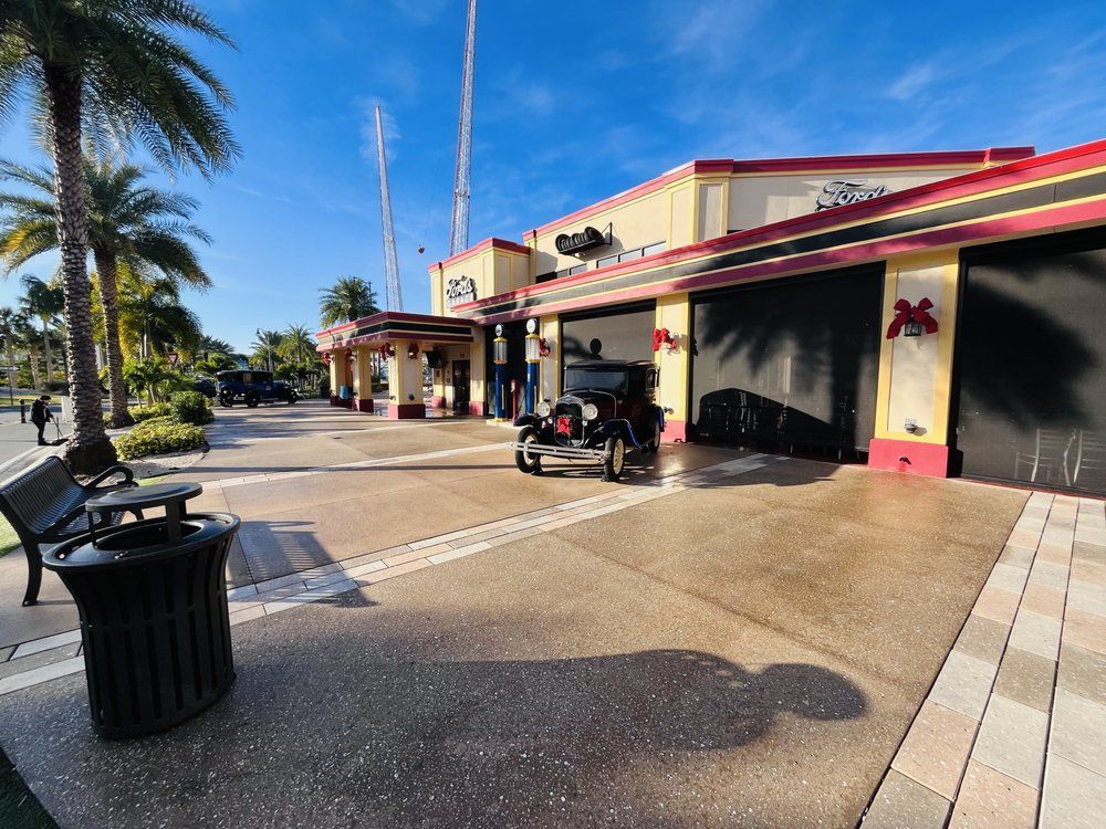 Exterior of a building with a red and yellow facade, black garage doors, and palm trees. A person on a scooter is in front.