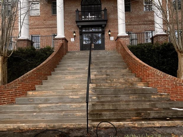 Brick building entrance with steps.  Half of steps are clean, half are dirty. Black railing and columns.