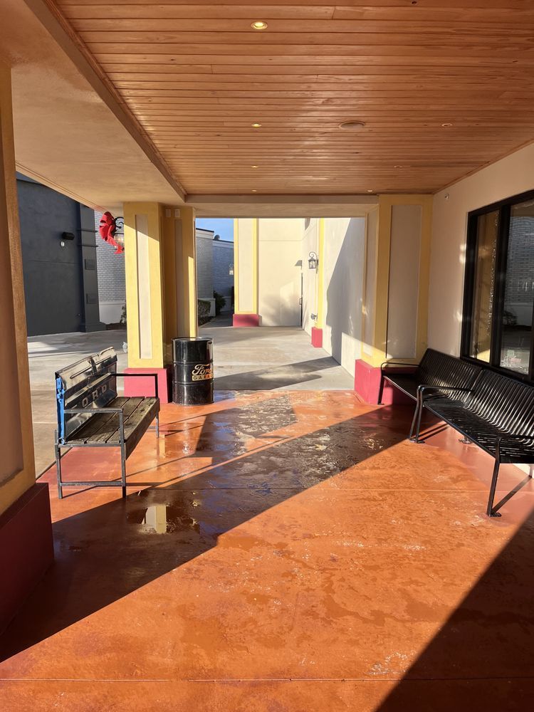 Covered outdoor patio with a bench, barrel, and open doorway leading to a sunlit courtyard. 