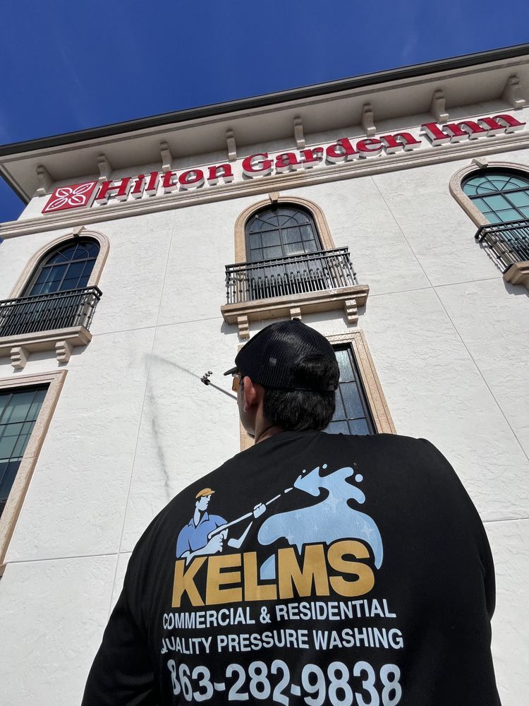 Man pressure washing a Hilton Garden Inn facade, wearing a black shirt with a 