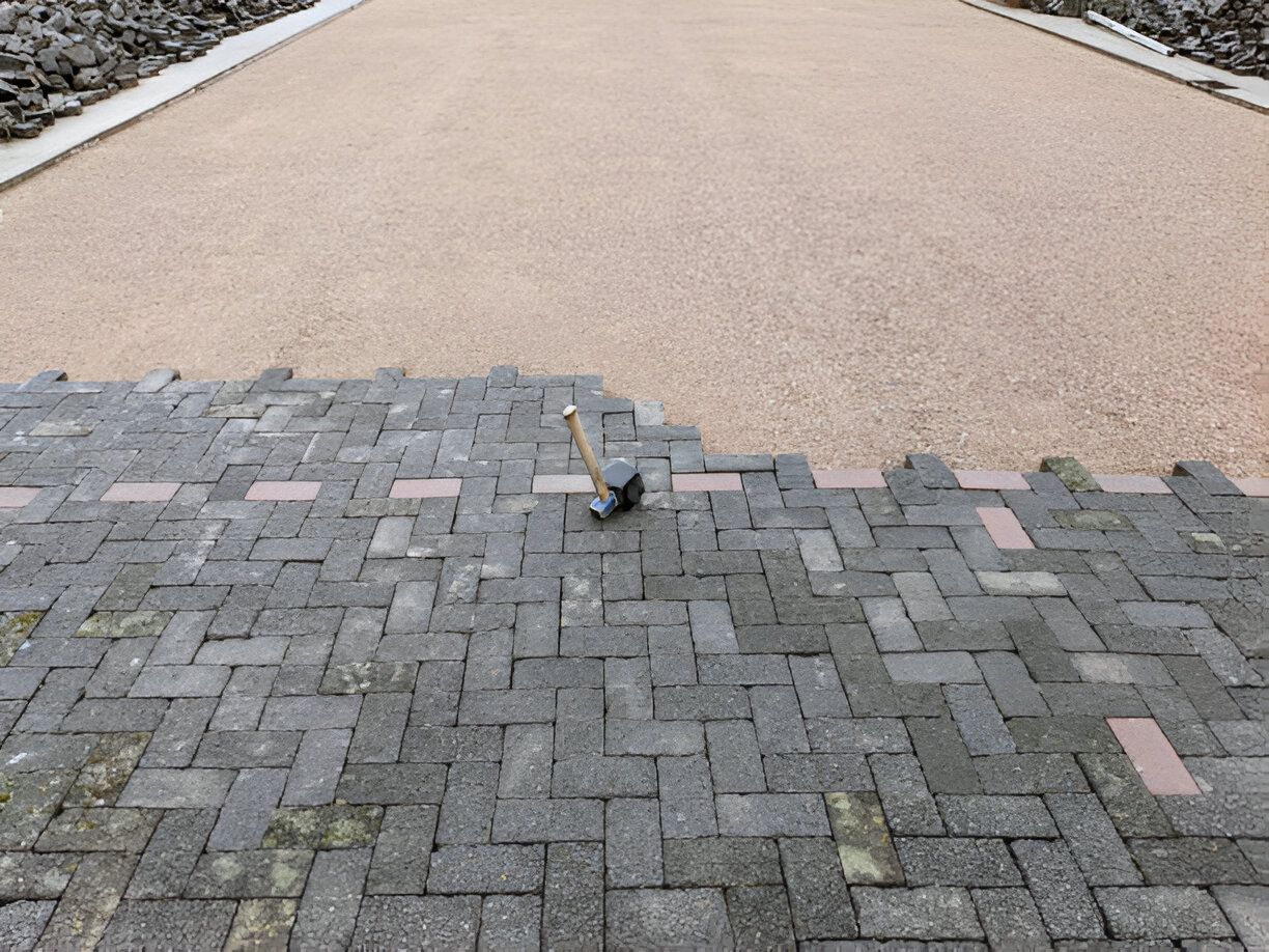 Pathway under construction; grey pavers being laid next to a tan gravel surface, with a hammer on the pavers.