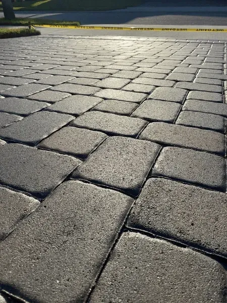 Close-up of gray brick pavers on a driveway, with yellow caution tape in the background.