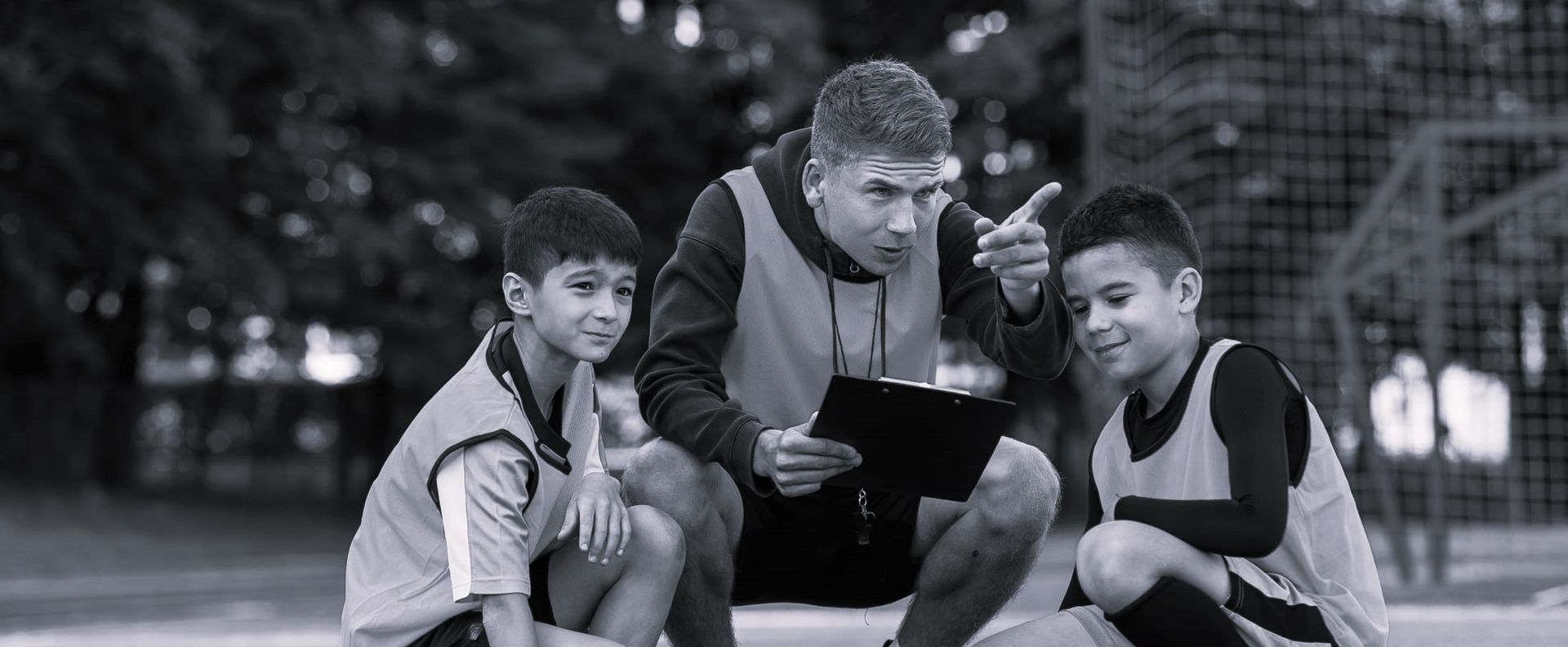 A man is talking to two young boys on a soccer field.