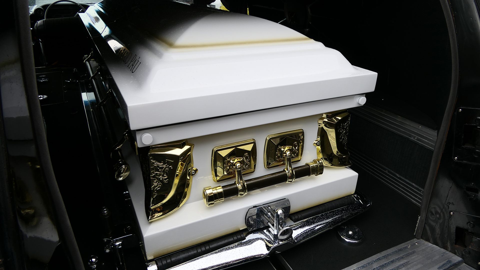 a white coffin with gold trim sits in the back of a car