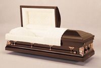 a brown coffin with the lid open and a white blanket on it .