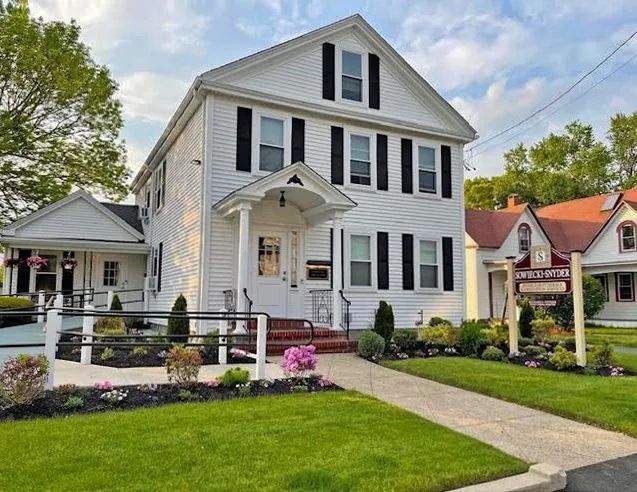 a large white house with black shutters is sitting on top of a lush green lawn .
