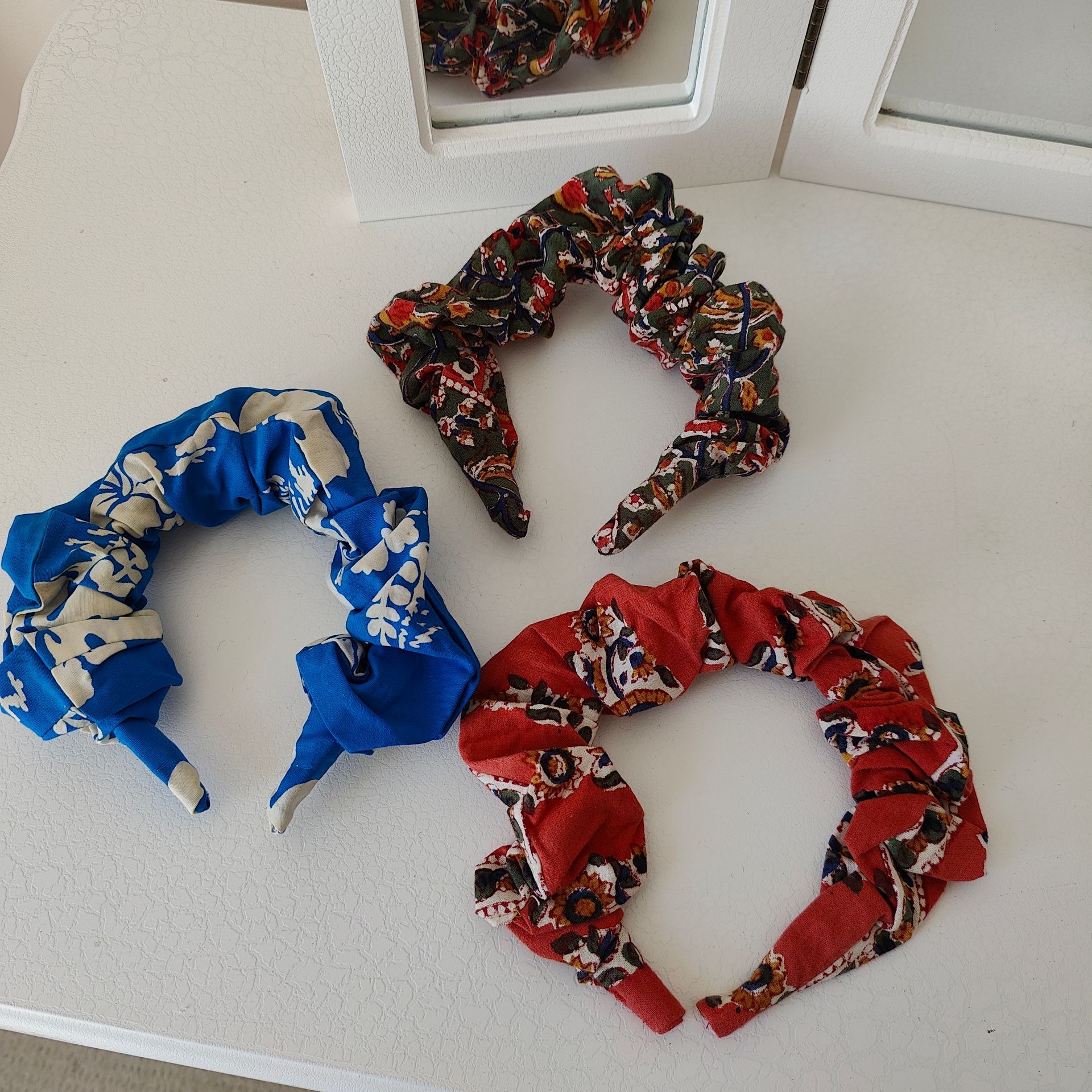 three floral fabric scrunchie
headbands next to a mirror