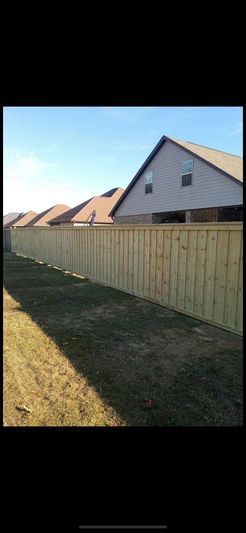 A wooden fence surrounds a residential area with a house in the background.