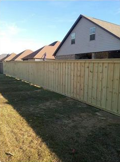 A wooden fence surrounds a residential area with a house in the background.