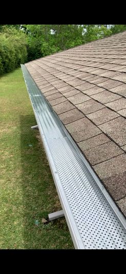 A gutter is sitting on top of a roof next to a grassy field.