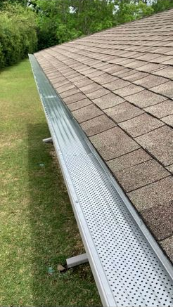 A gutter is sitting on top of a roof next to a grassy field.