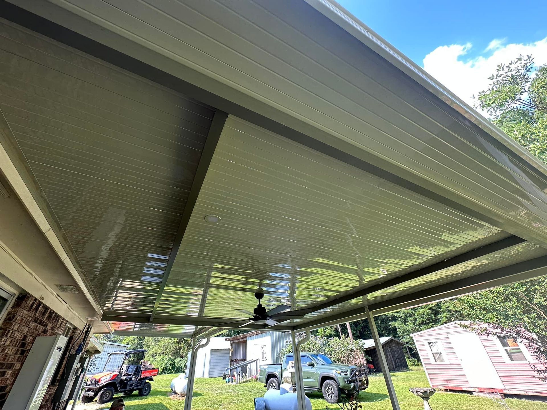 A ceiling fan is hanging from the ceiling of a carport.