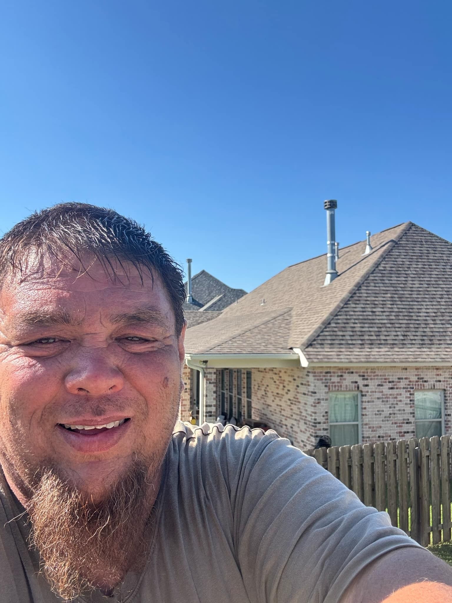 A man with a beard is taking a selfie in front of a house.